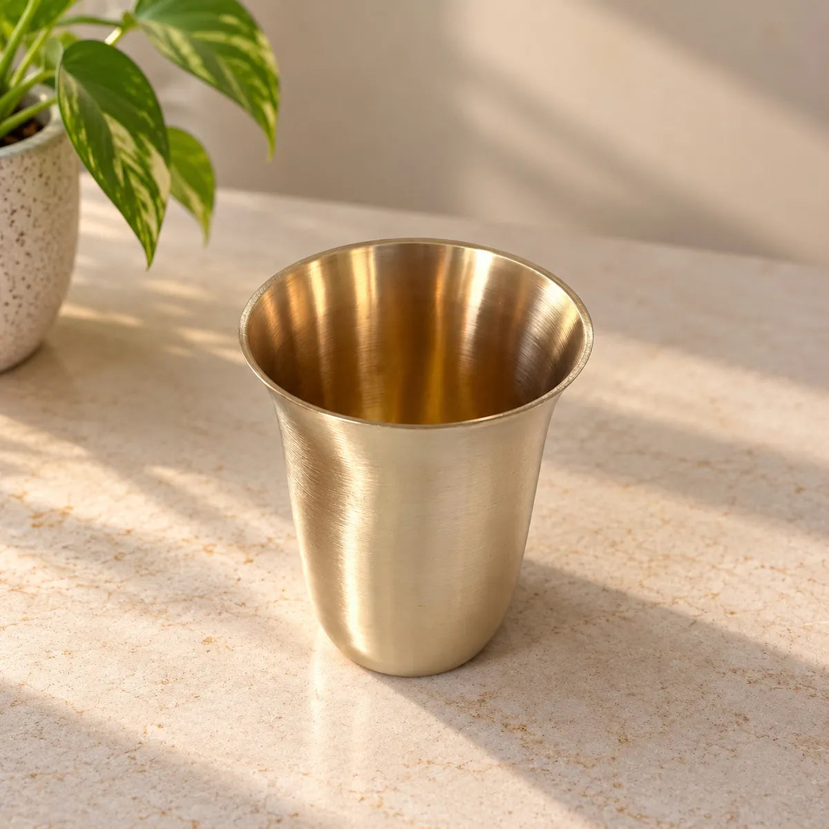 Kansa Glass Bangla bronze drinking glass with flared rim on marble counter. Zishta Drinkware